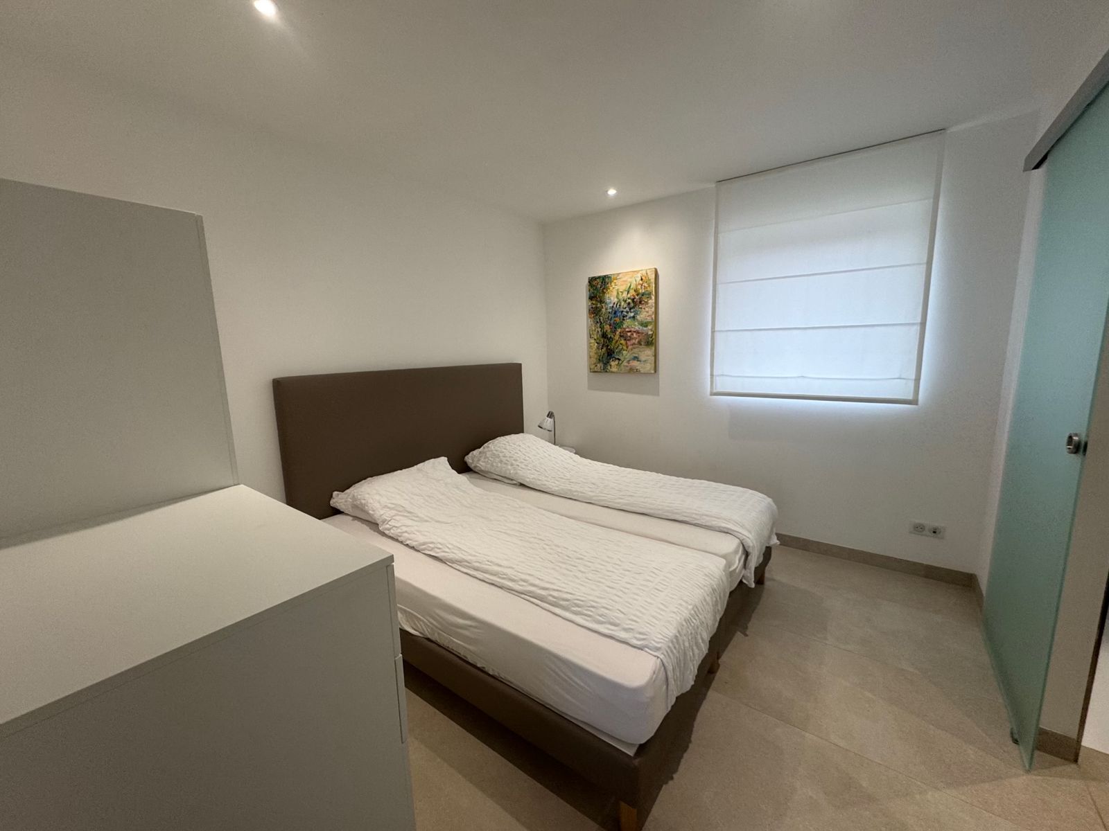 Chambre lumineuse avec lits, tableau et store à la fenêtre