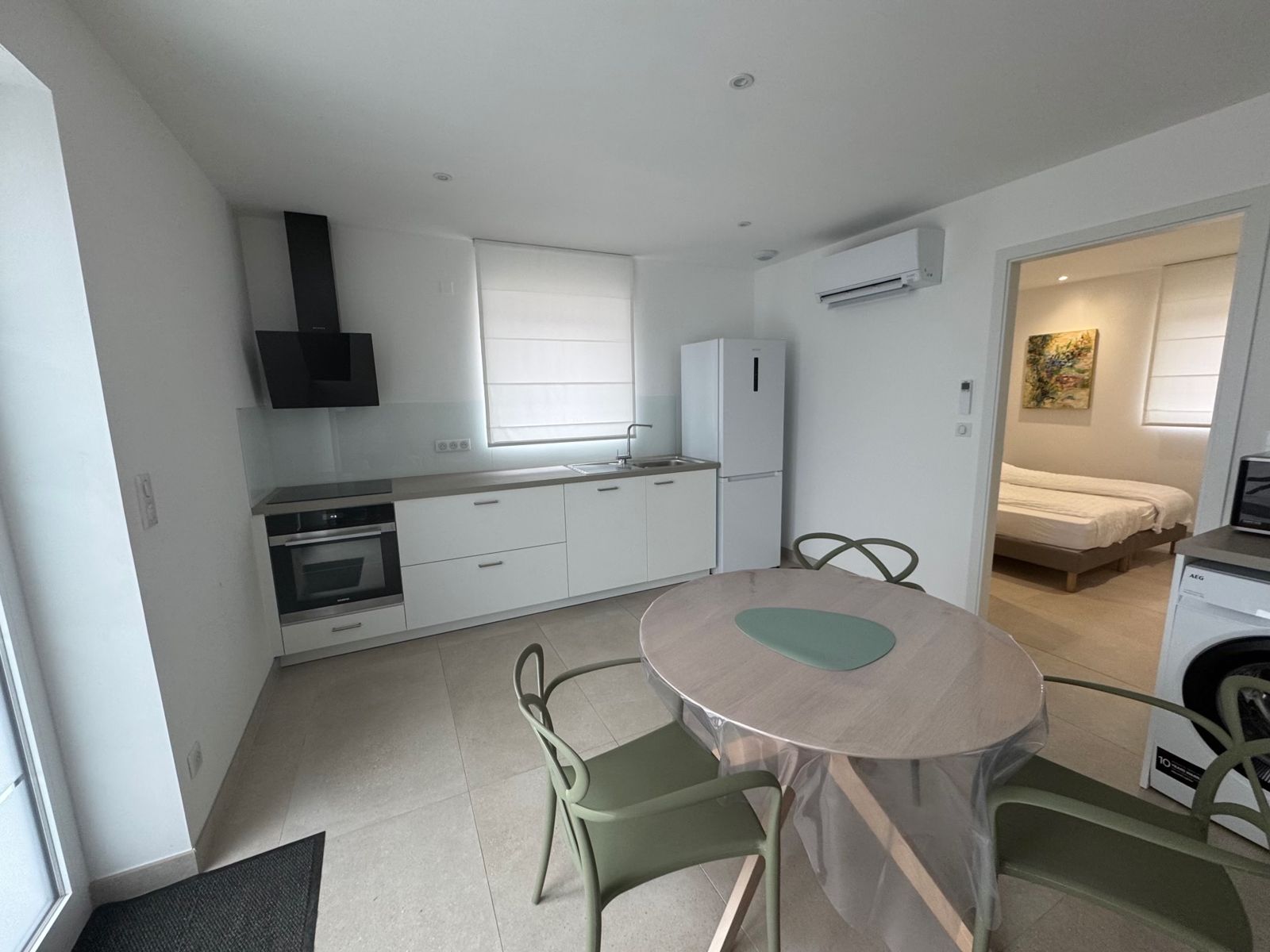 Pièce de vie lumineuse avec cuisine équipée, table et chaises, et chambre en arrière-plan