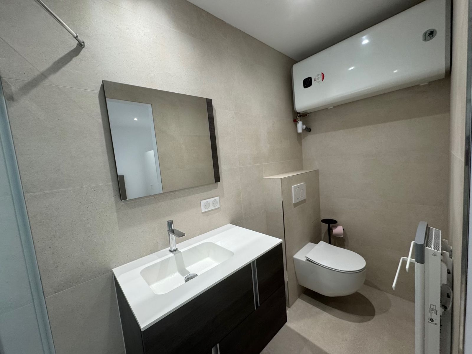Salle d'eau avec miroir, meuble vasque, WC suspendu et chauffe-eau